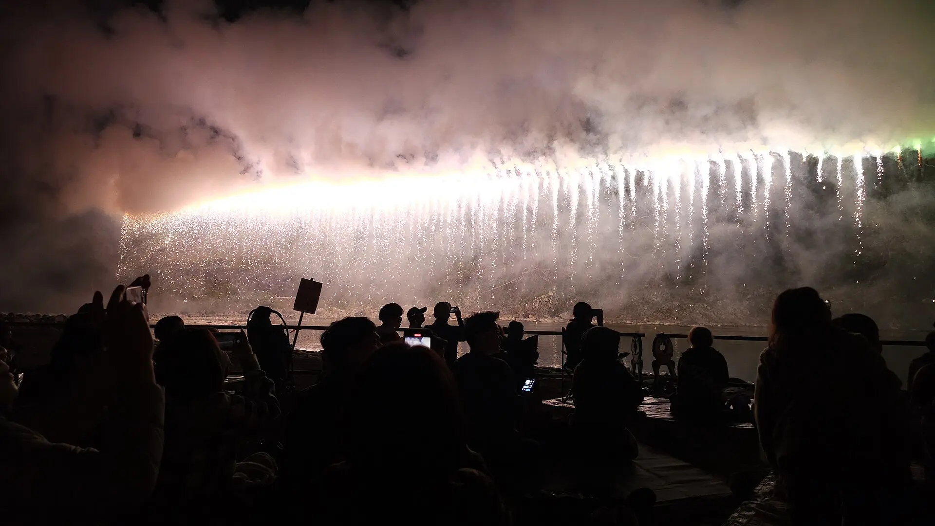 煙の中に流れ落ちる光を見つめる観客のシルエット(やまびこ花火大会)