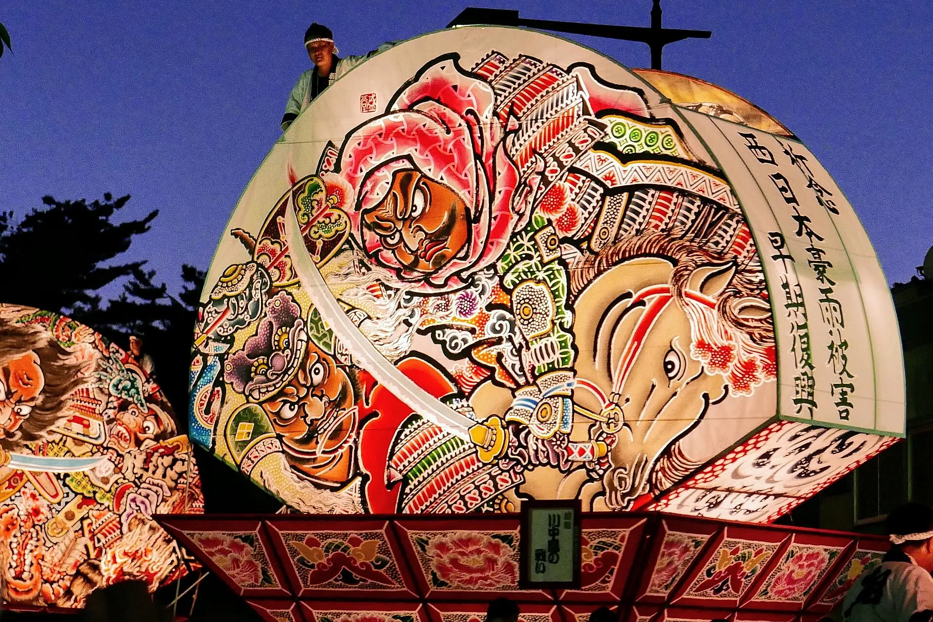 夕暮れの青い空に灯る、武者と馬を描いた扇ねぷた
