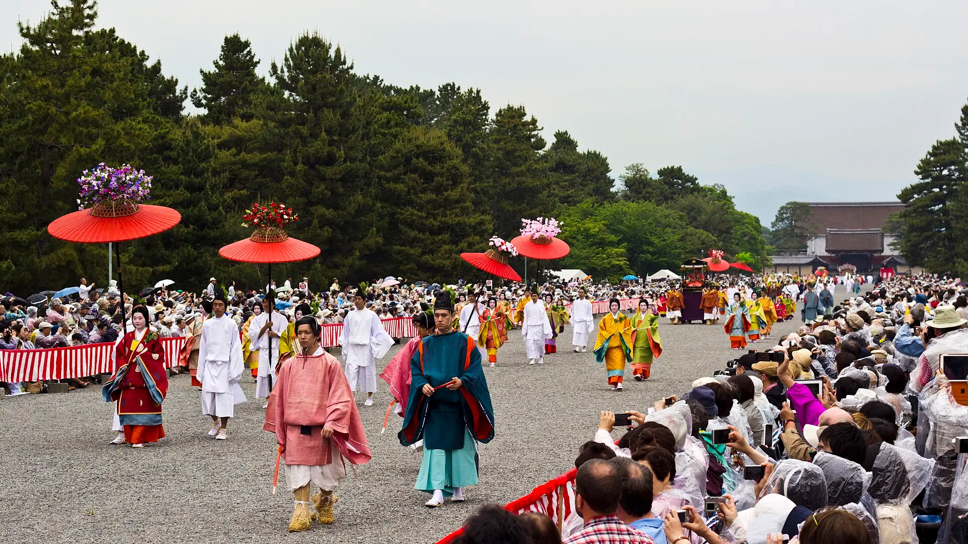 京都御所の砂利道を進む平安装束と朱傘の葵祭行列
